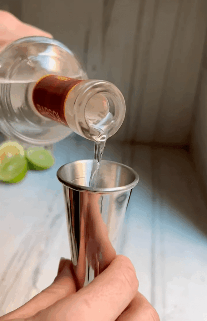 pouring pisco into a cocktail jigger for a pisco sour.