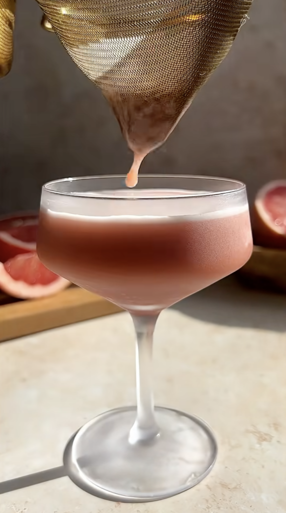 pouring a winter negroni sour into a coupe glass