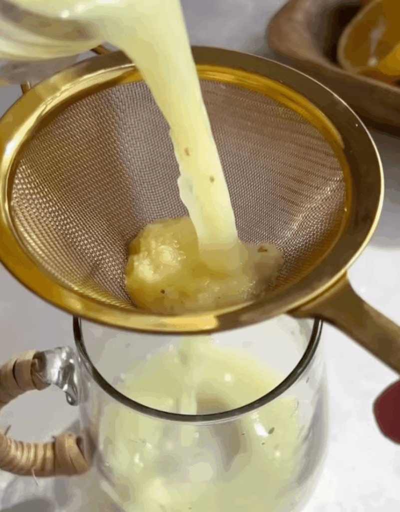 Homemade ginger juice being poured through a fine mesh sieve